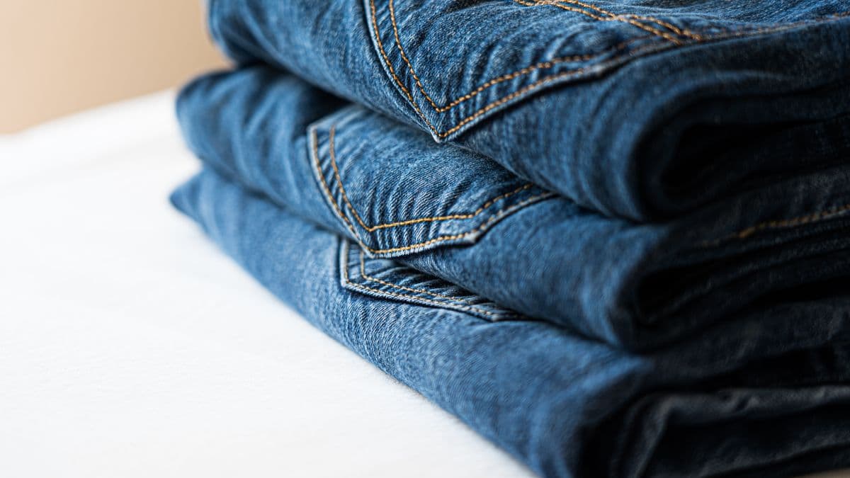 A neat stack of folded blue denim jeans showing stitching and texture